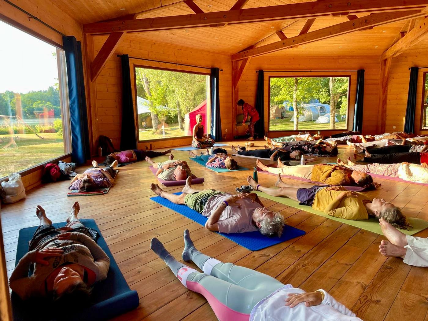 Un groupe en relaxation finale dans une grande salle en bois ouverte sur la nature