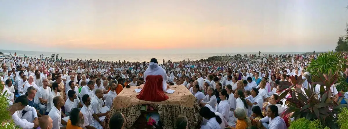 Au coucher du soleil, Amma assise face à une foule vêtue de blanc, au bord de la mer à Amritapuri