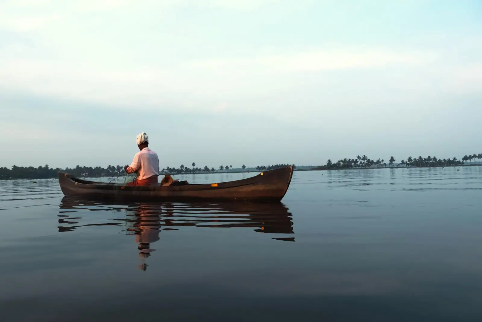 Pêcheur du Kérala dans sa barque, sur l'eau calme des backwaters à l'aube