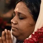 Amma, les mains jointes, une guirlande de fleurs rouges sur l'épaule